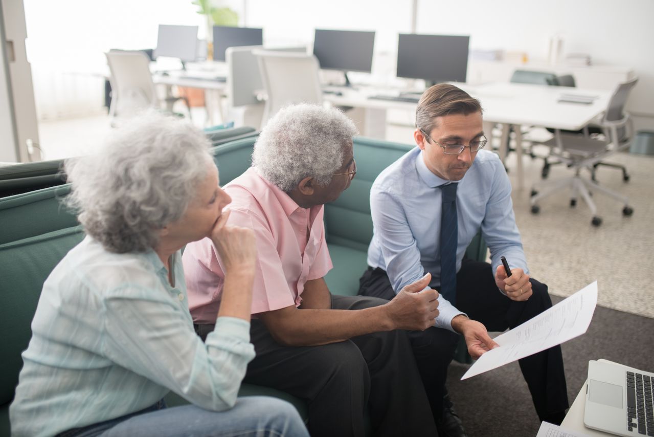 Tax professional consulting with elderly clients in an office, paperwork visible on the desk