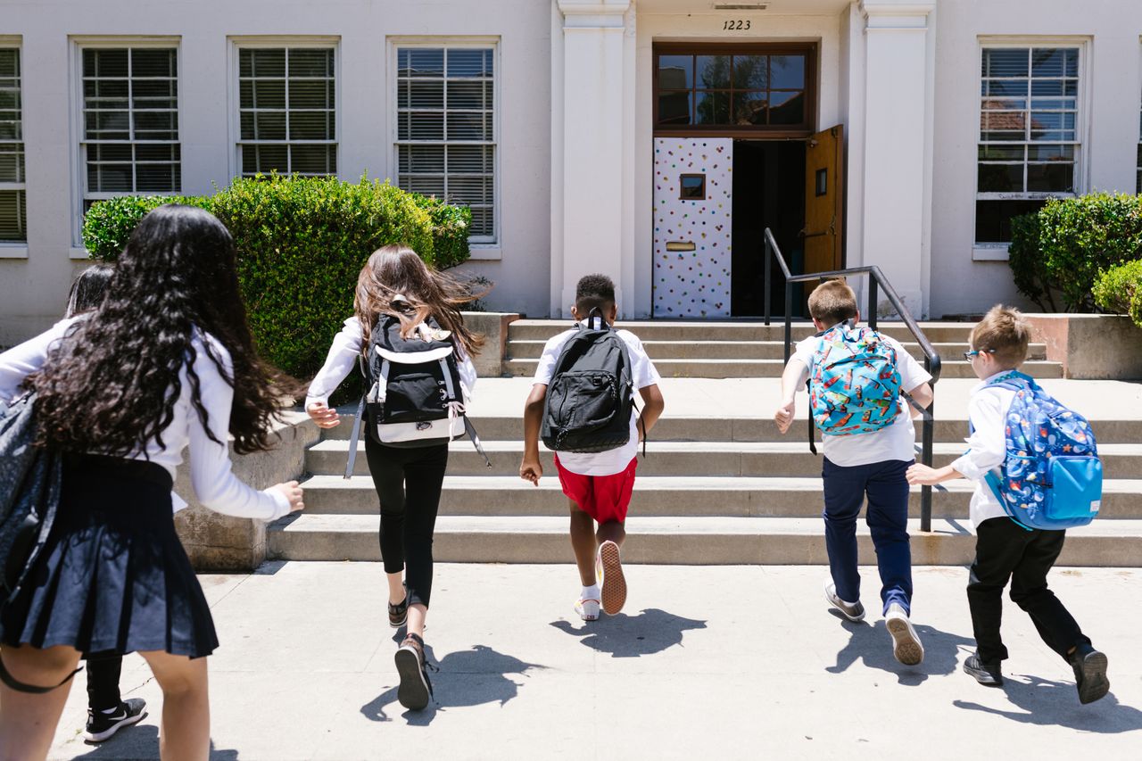Students with backpacks running into school, viewed from behind