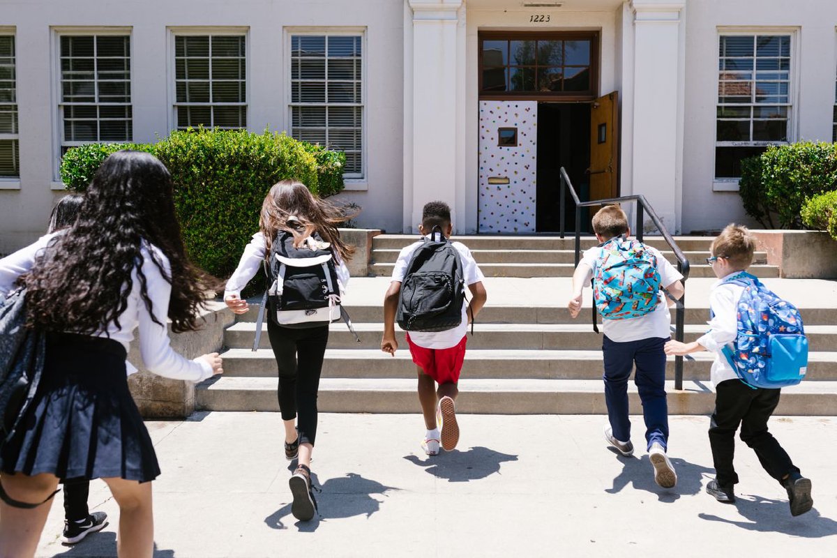 Students with backpacks running into school, viewed from behind