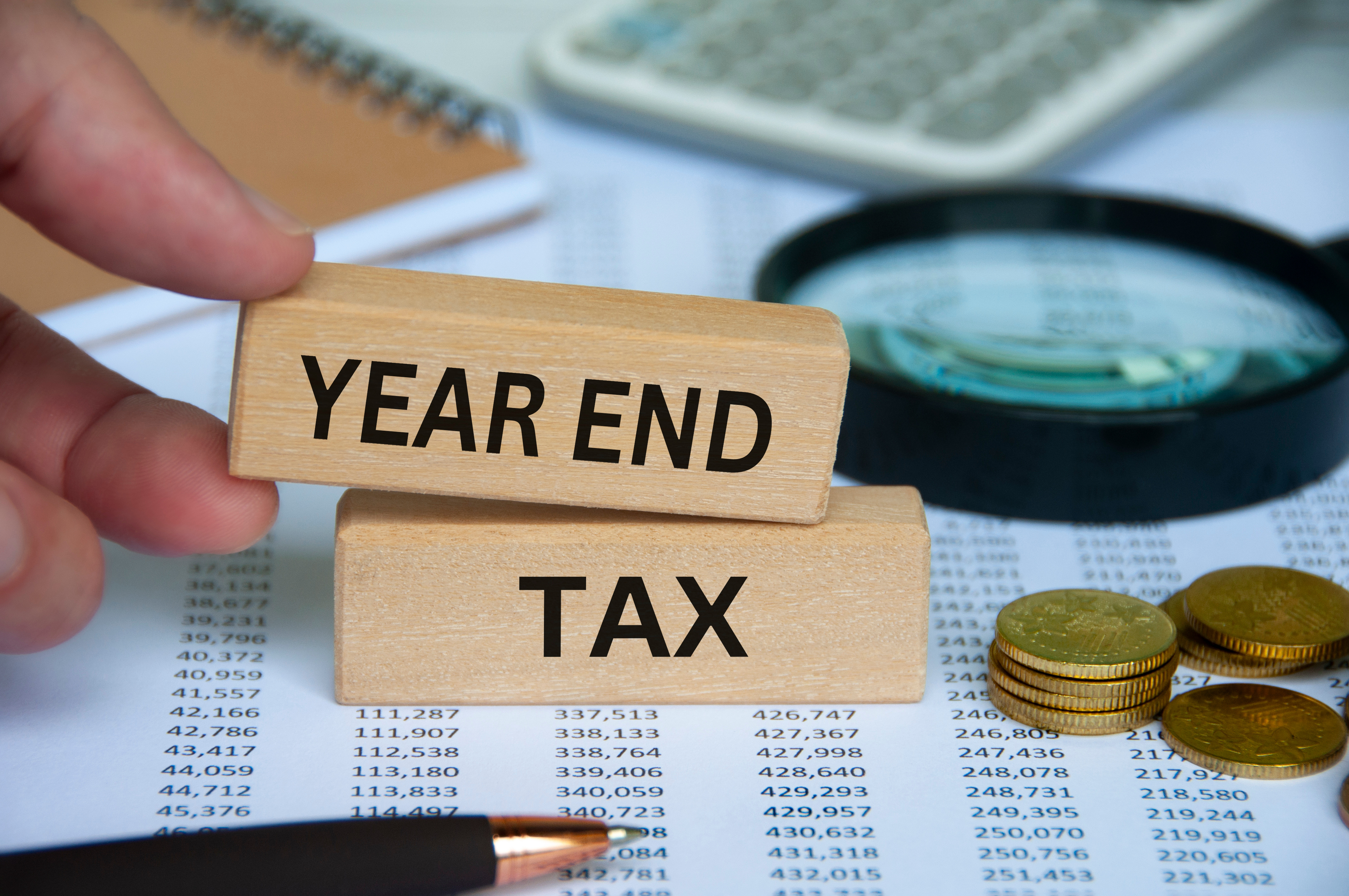Year end tax text on wooden block with pen, notepad, calculator and coins background