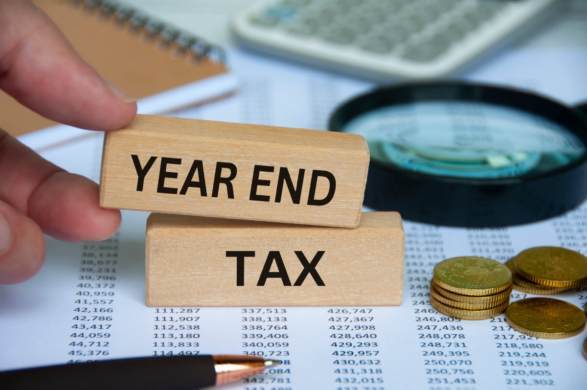 Year end tax text on wooden block with pen, notepad, calculator and coins background