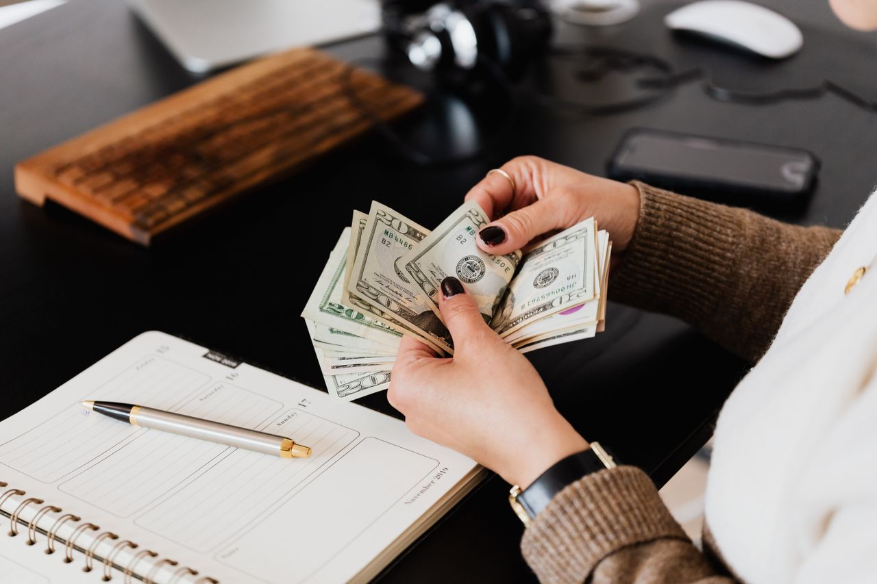 Person counting cash next to a planner and gold pen on a desk