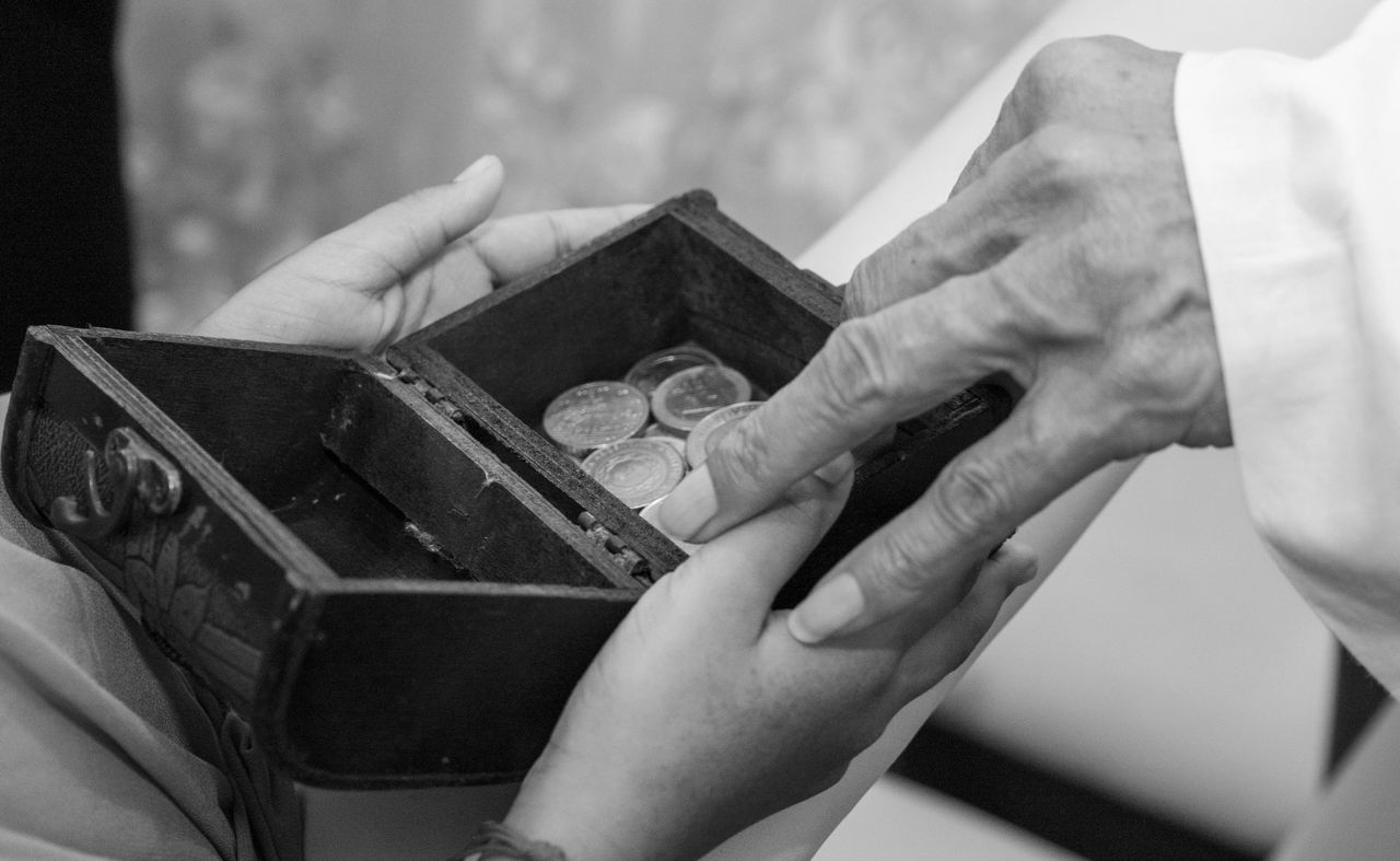 Hands exchanging coins in a small wooden box, representing a family inheritance
