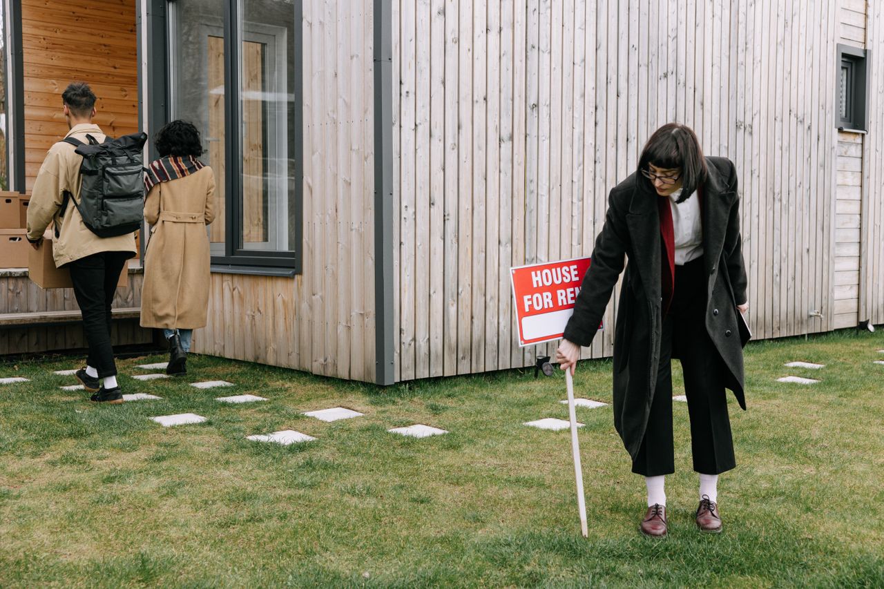 A couple moving into a new rental home while a real estate agent removes a for-rent sign from the yard